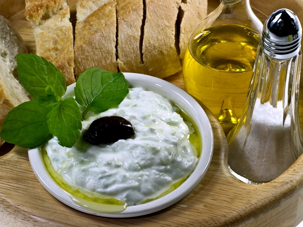Tzatziki served in a bowl with olive oil, a black olive and fresh mint, alongside sliced bread.