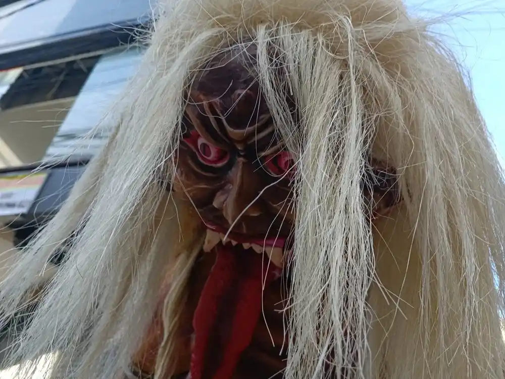 Ogoh-ogoh sculpture in Kuta, Bali, depicting a fierce mythical figure with red eyes, sharp teeth, a long red tongue and long white hair.