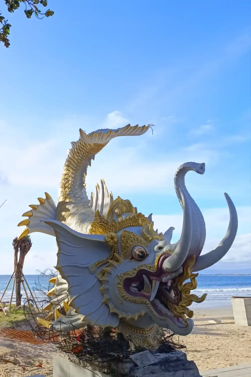 Traditional Balinese sculpture on Kuta Beach (Pantai Kuta) in Bali, depicting a mythical creature with ornate gold details beside the sea.