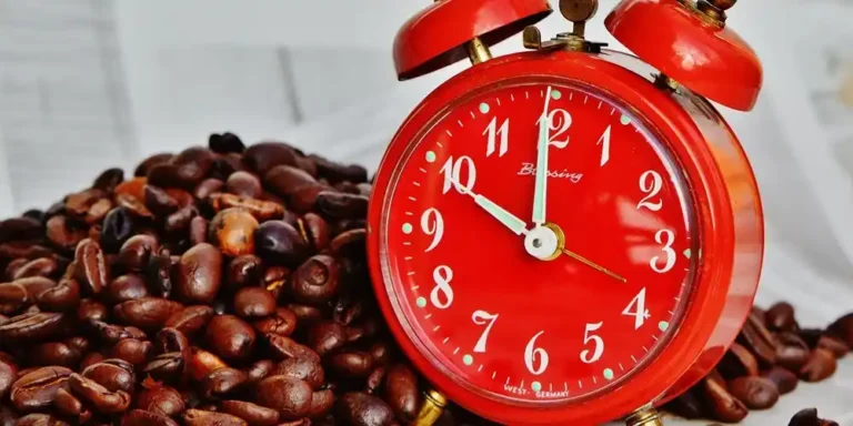 Red vintage alarm clock resting on roasted coffee beans, symbolising the relaxed pace of the Santai lifestyle.
