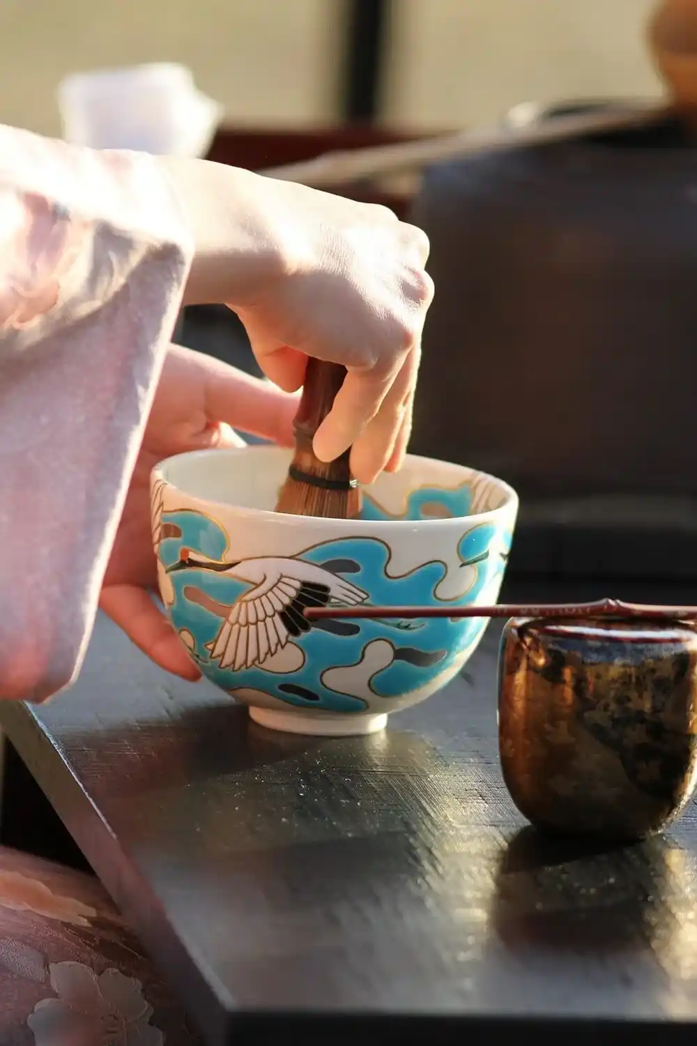 Traditional Japanese tea preparation with a bamboo whisk in a decorated ceramic bowl.