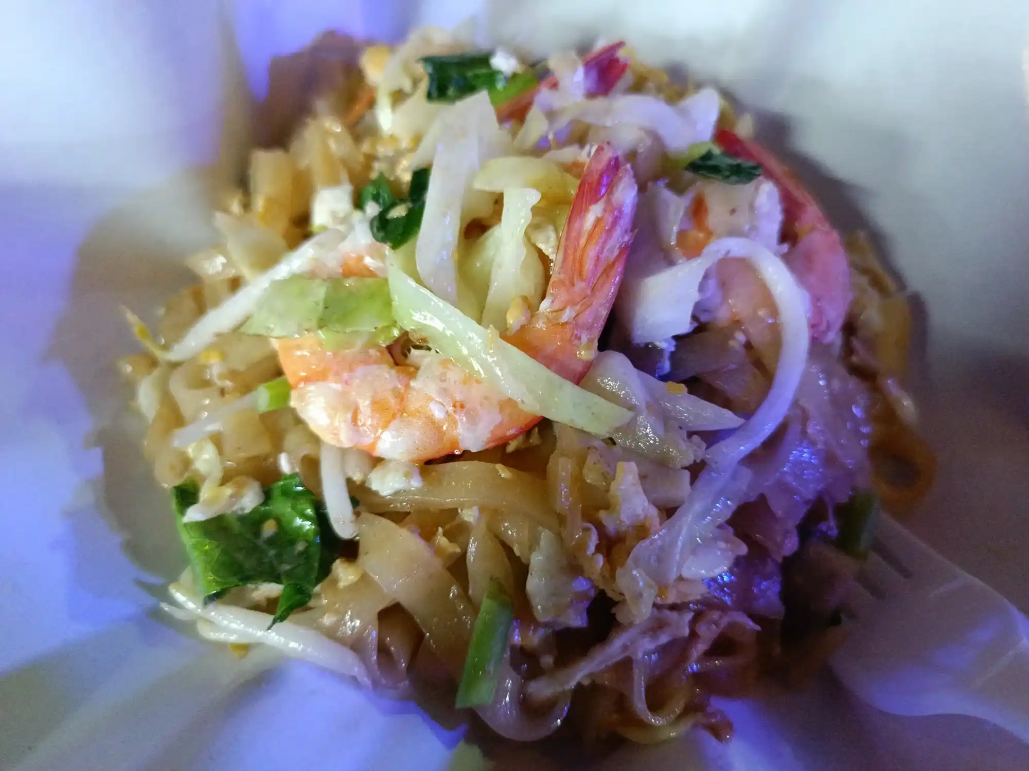 Tampak dekat Pad Thai dengan udang, kwetiau, telur orak-arik, tauge, dan daun bawang dalam wadah putih.