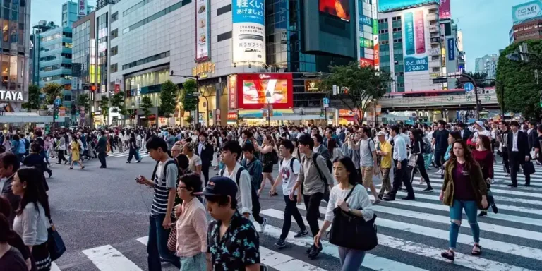 Tokyo’s Shibuya Crossing filled with pedestrians, surrounded by busy streets, shops and illuminated advertising signs.
