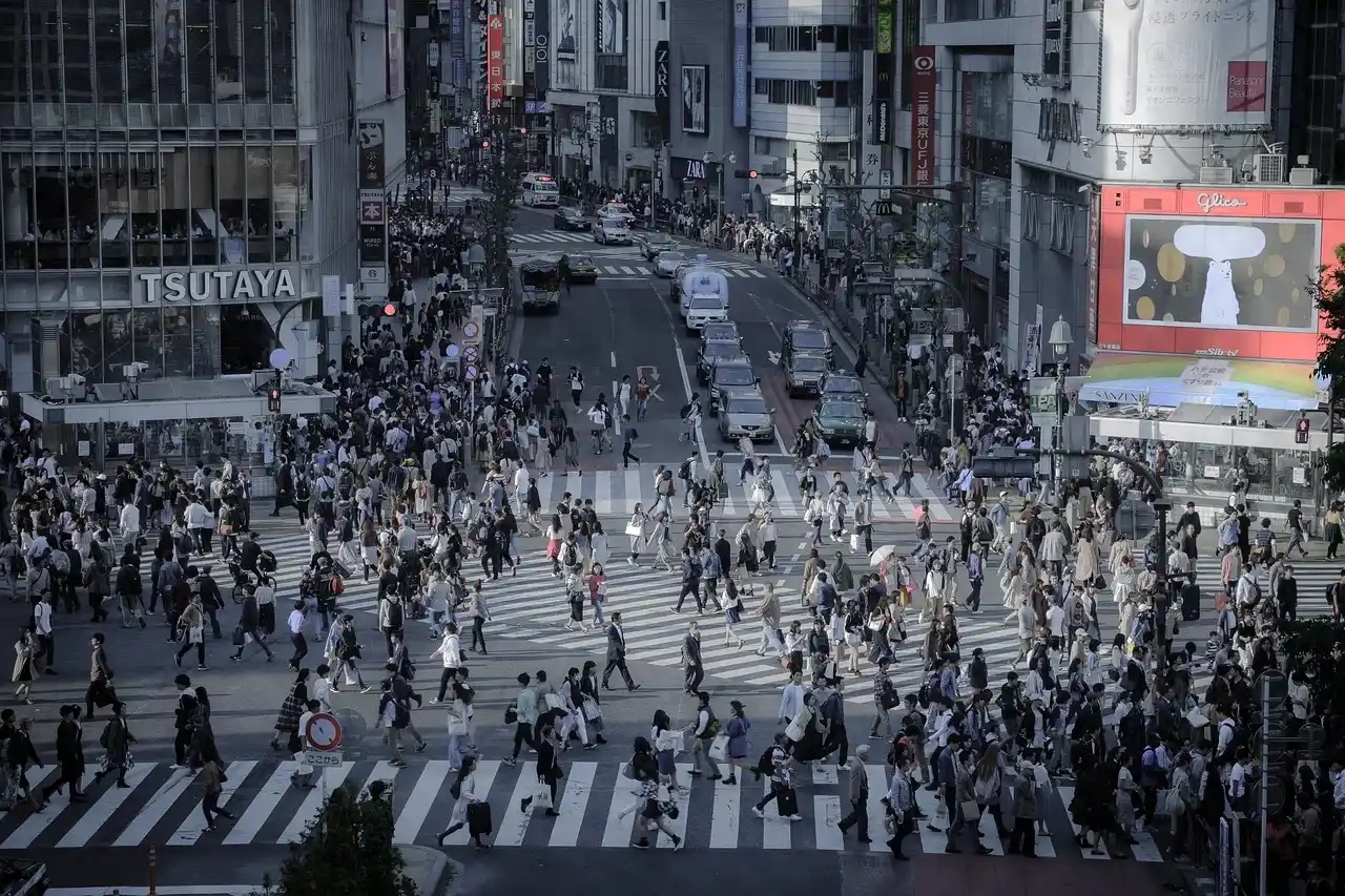 Shibuya Crossing in Tokyo crowded with pedestrians, traffic and surrounding shops and digital billboards.