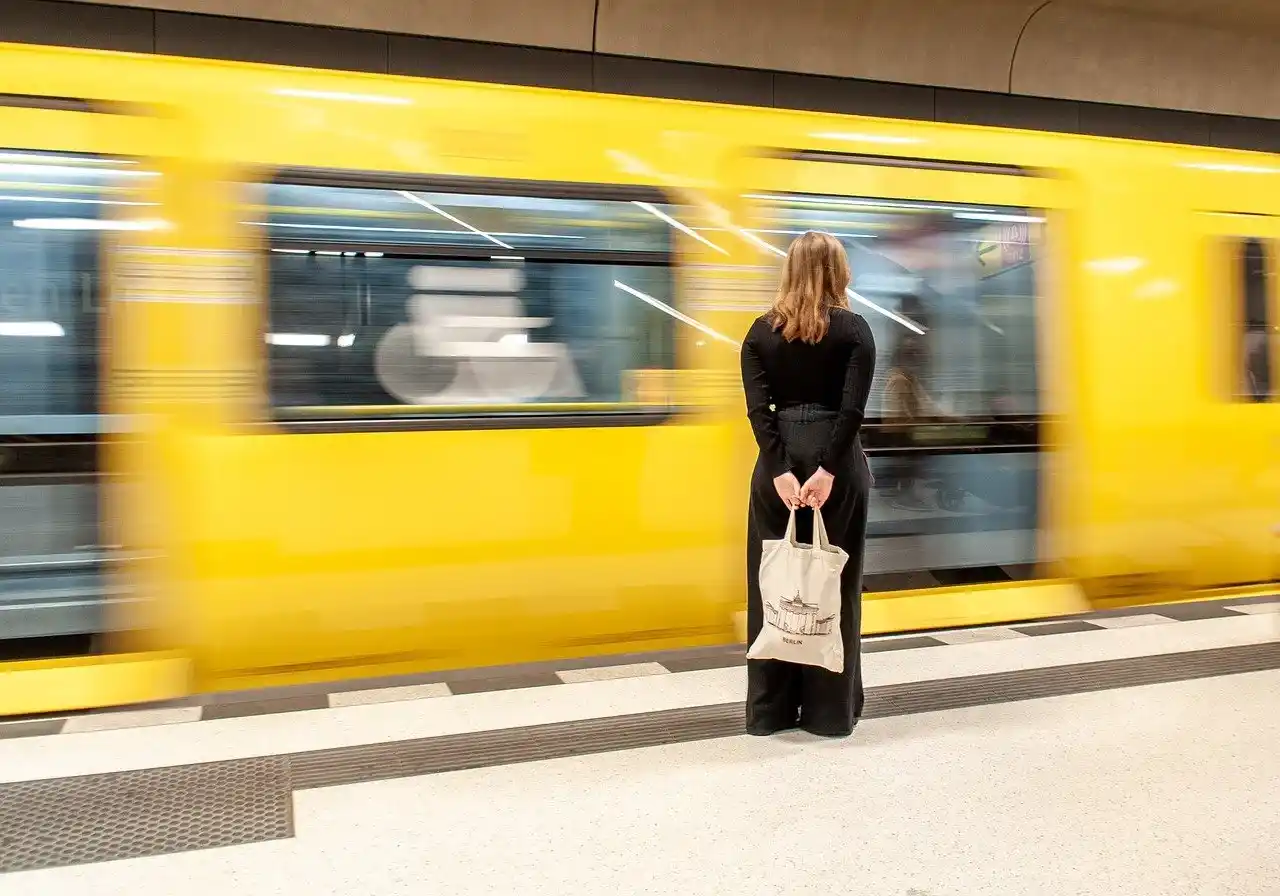 Woman standing on a Tokyo train platform as a yellow commuter train speeds past.