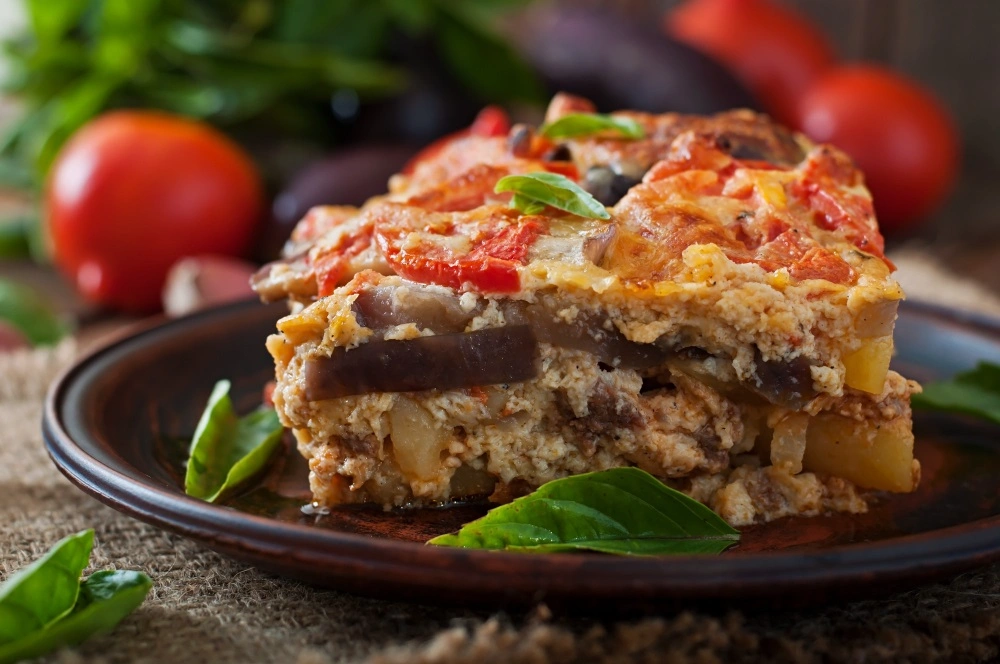 Moussaka Yunani tradisional dengan lapisan terong, daging dan béchamel yang disajikan di atas piring.