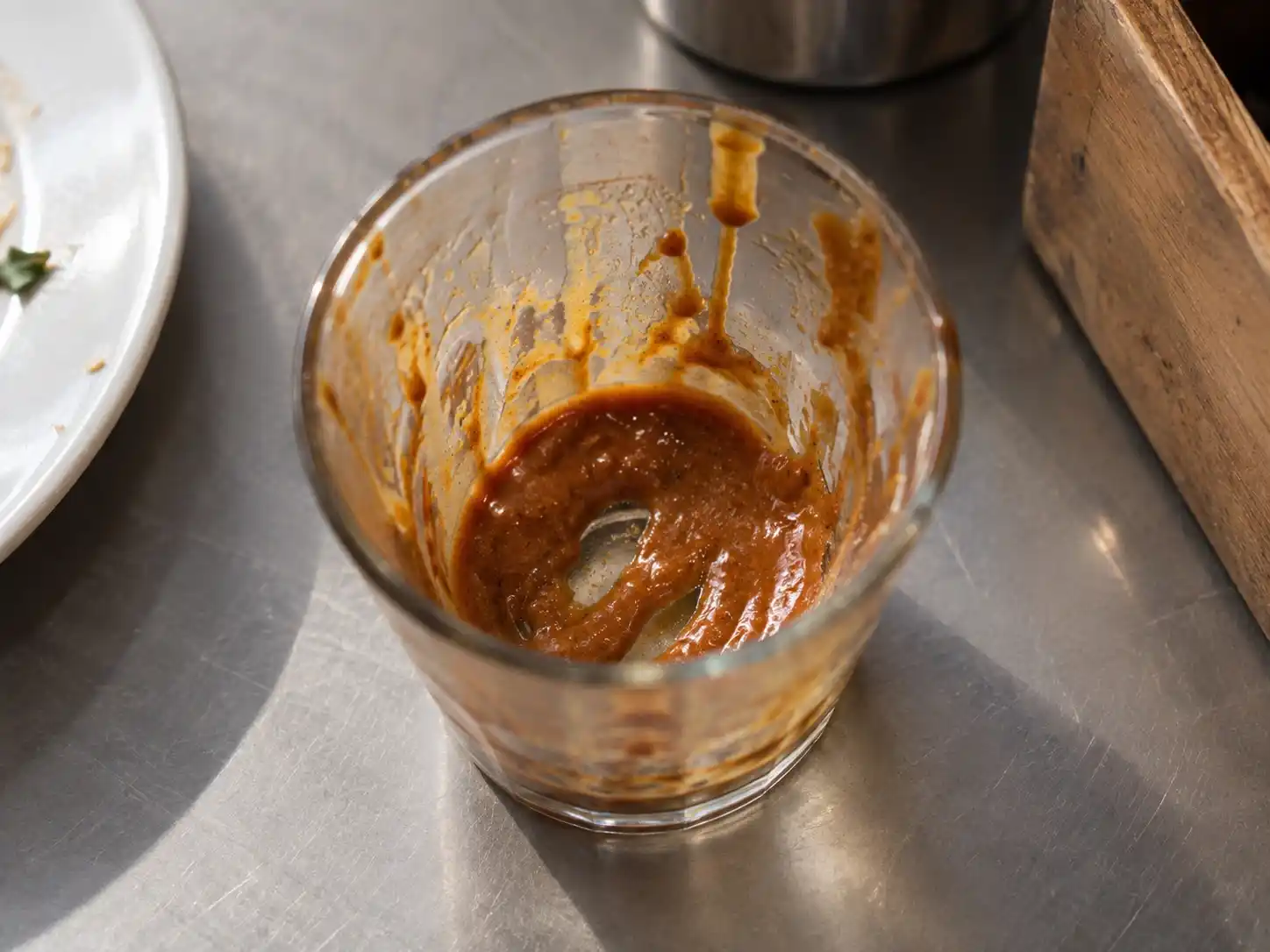 A clear glass in daylight with slow streaks of sauce or liquid inside.