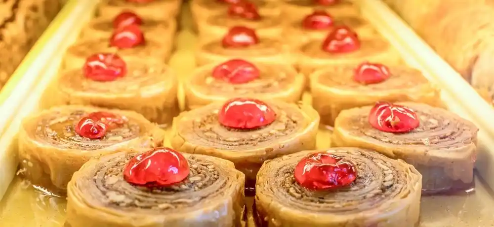 Traditional Greek Baklava with nuts and syrup topped with cherries in a pastry display.