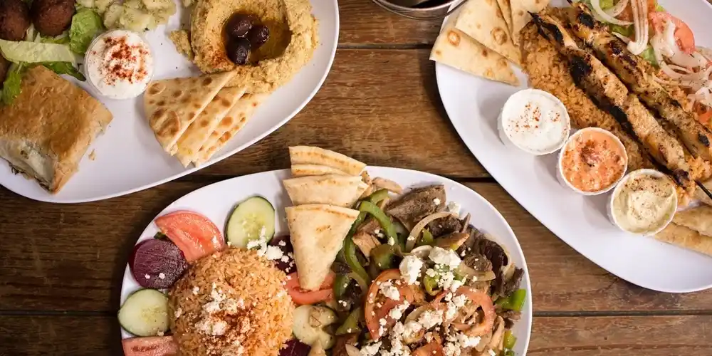 Greek food spread in Corfu with souvlaki, pita, dips and grilled meat on a wooden table.