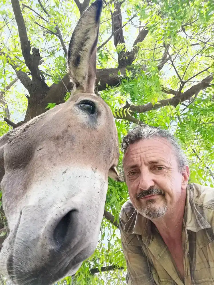 Luc Triekels poses beside a donkey under a leafy tree at Sandicoly Ecofarm in Senegal.