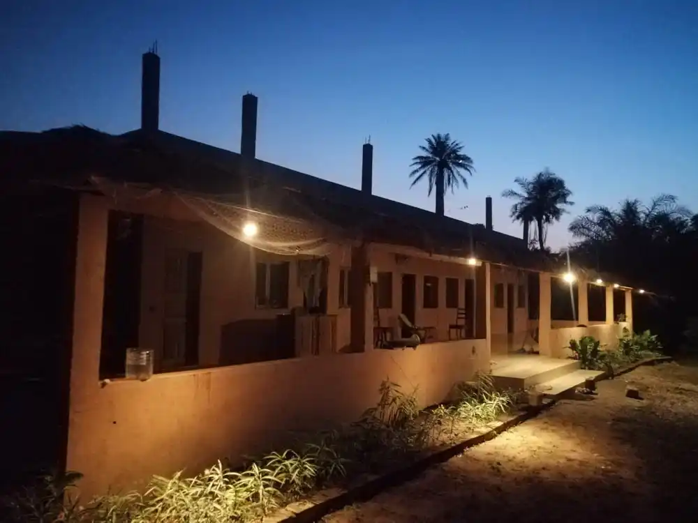 The cabins at Sandicoly Ecofarm in Senegal, illuminated at dusk with palm trees silhouetted against the evening sky.