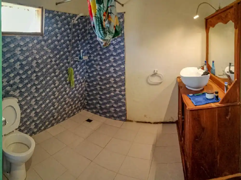 Bathroom inside one of the cabins at Sandicoly Ecofarm in Senegal, with a tiled shower area, toilet and wooden vanity with a washbasin.
