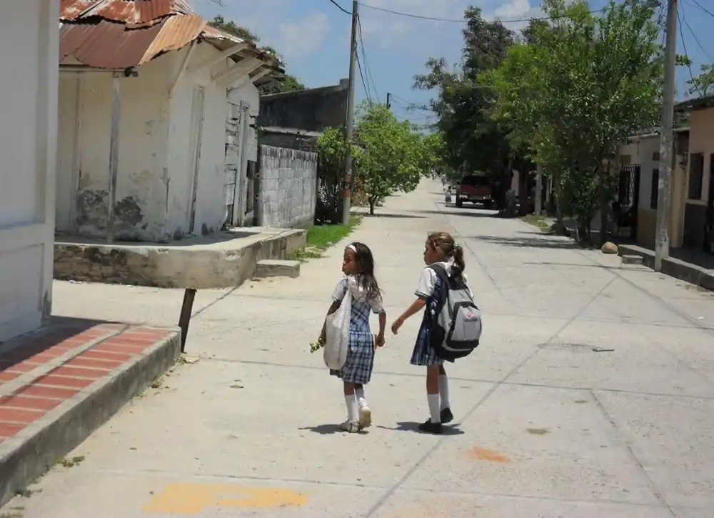 Schoolchildren walking in a street in Aracataca Colombia with houses and trees around.