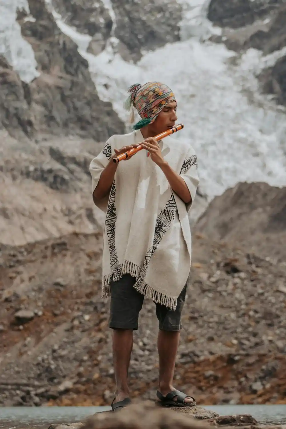 Man in traditional Andean clothing playing a wooden flute in a mountainous landscape in Peru.