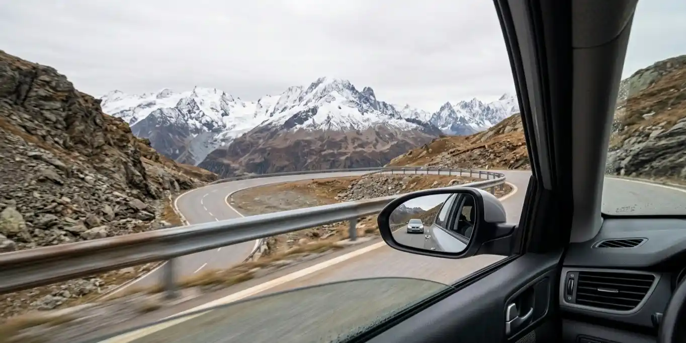 View from car driving on a winding mountain road with snow-covered peaks in the distance.