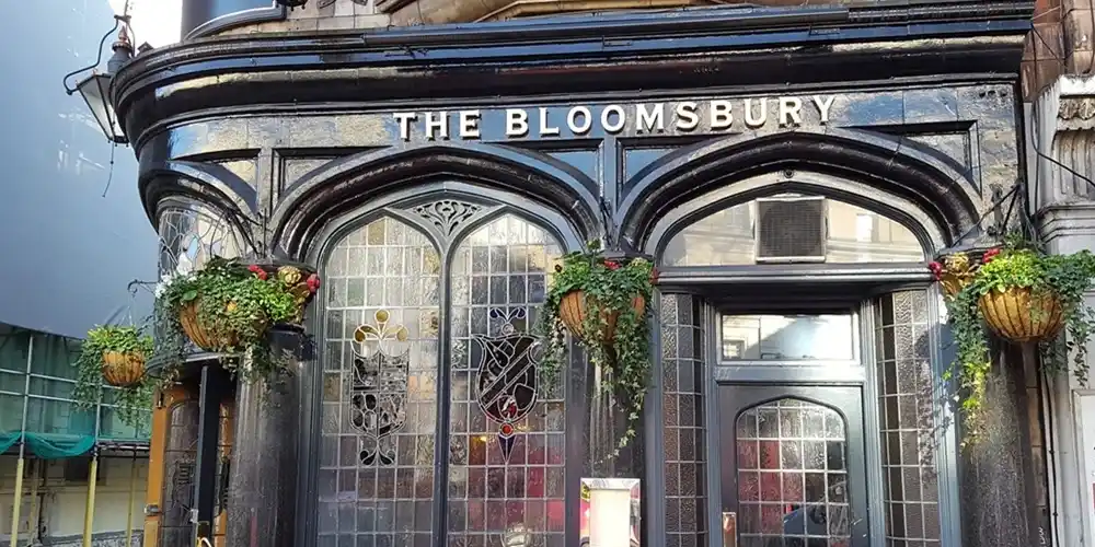 Historic Bloomsbury pub in London with dark wood facade, arched windows and hanging plants.