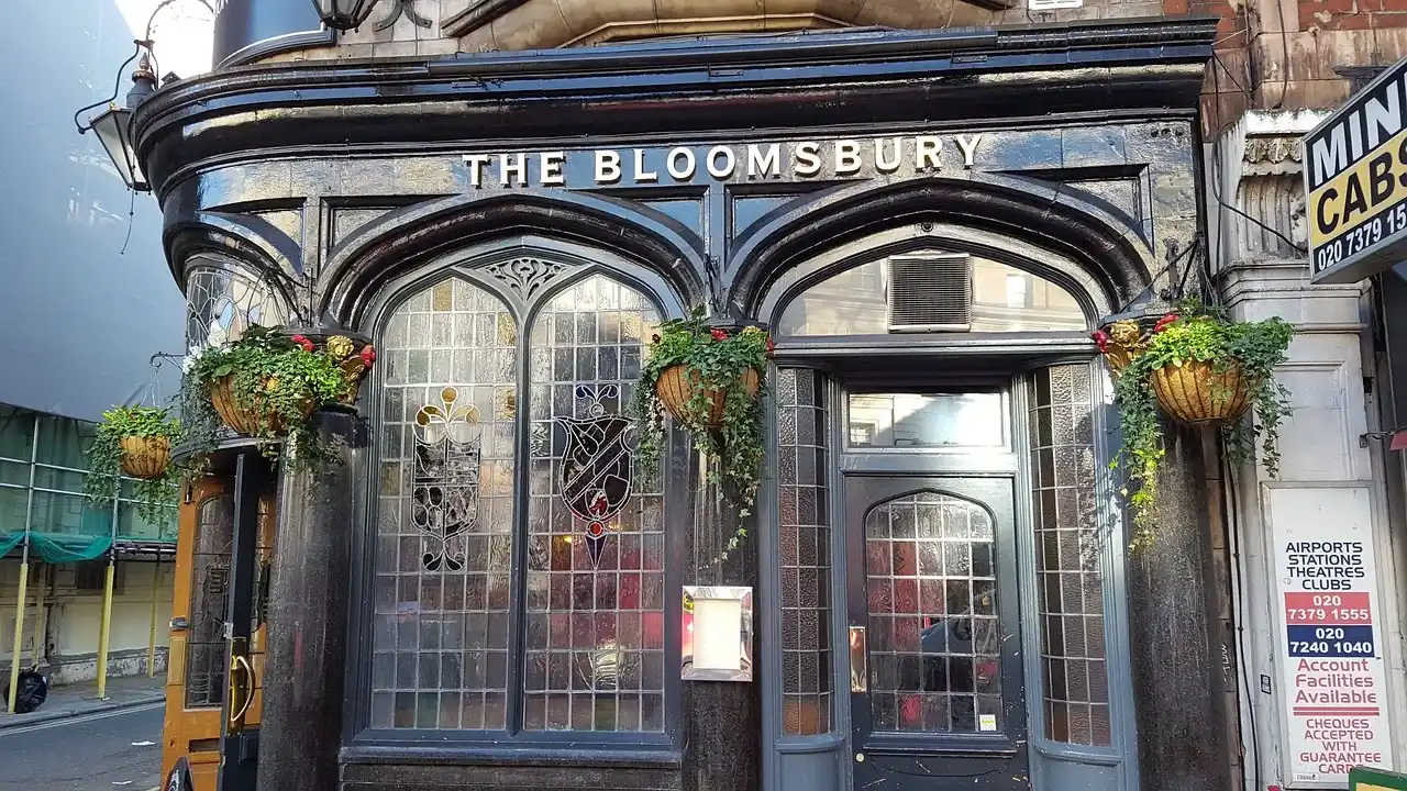 Historic Bloomsbury pub in London with dark wood facade, arched windows and hanging plants.