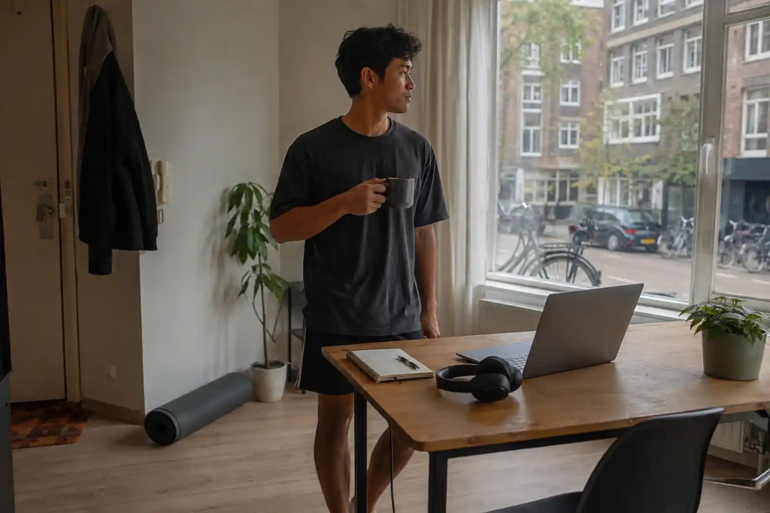 Pria digital nomad minum kopi di dekat laptop setelah berolahraga pagi di apartemen Amsterdam.