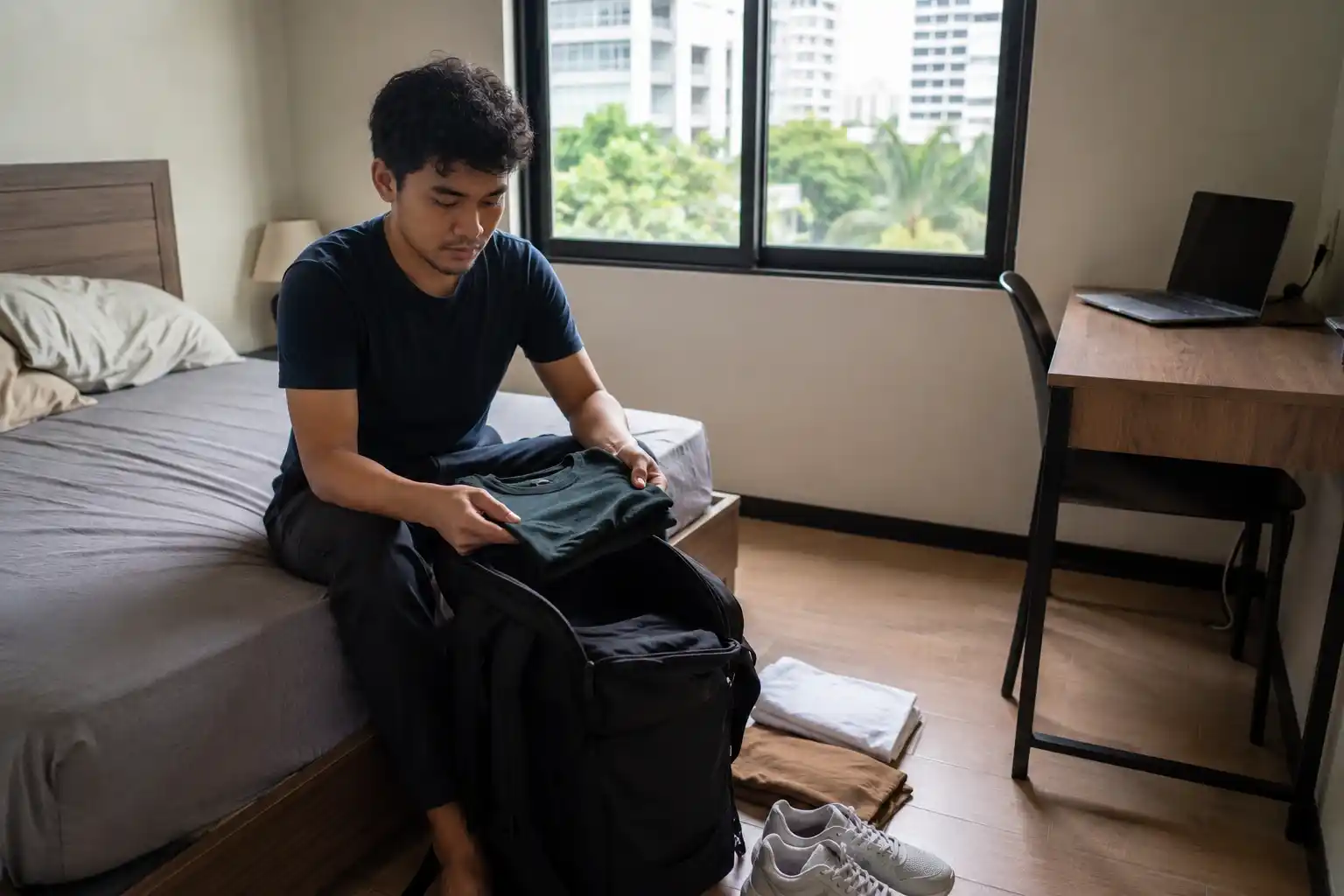 Pria digital nomad membongkar pakaian dari ransel di kamar sementara di Bangkok.
