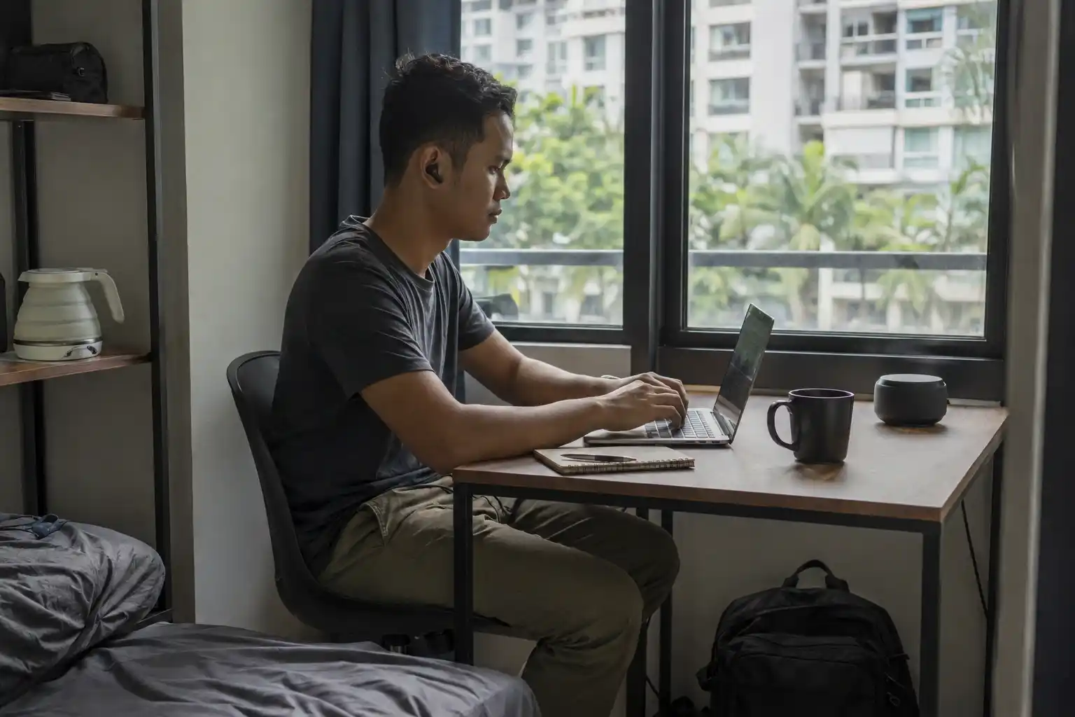 Pria digital nomad bekerja dengan laptop dan barang-barang portabel di apartemen sewaan di Kuala Lumpur.