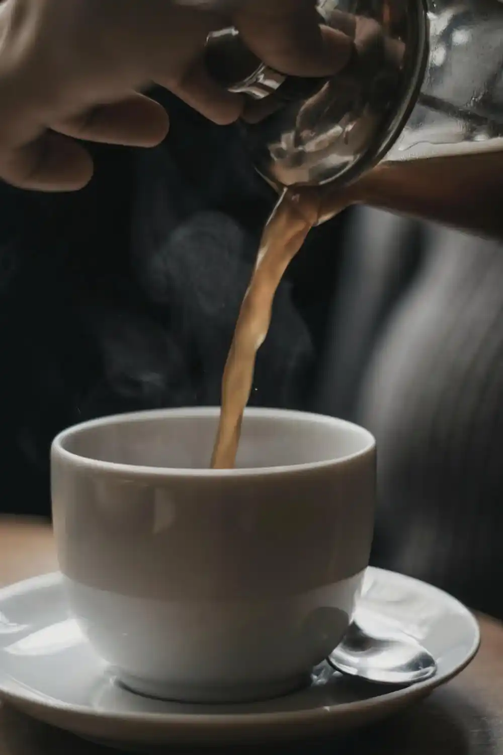 Coffee being poured from a metal server into a white cup.
