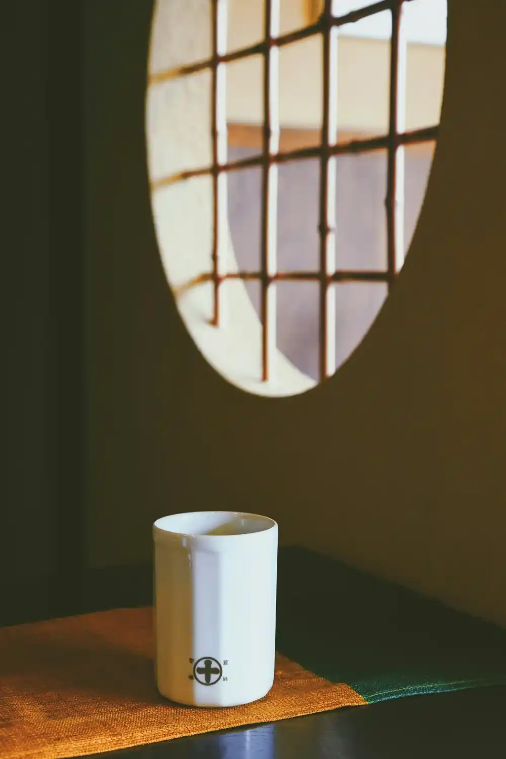 White coffee cup on a wooden table with the shadow of a traditional window falling across the wall in Kyoto.