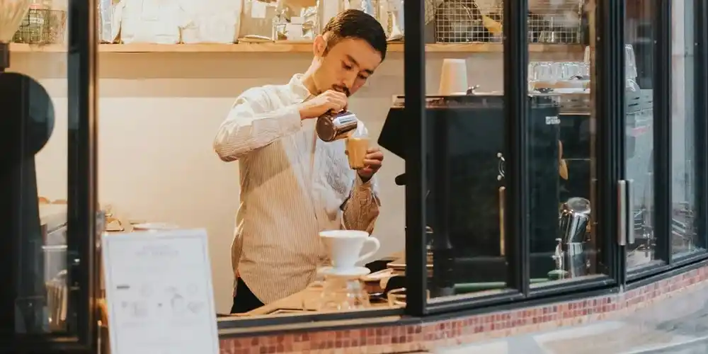Tokyo barista carefully pouring coffee into a cup behind the counter of a modern café.