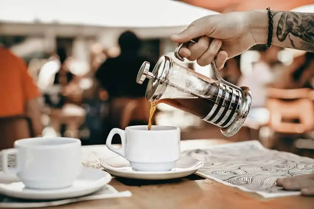 Coffee being poured into a white cup at a busy cafe.